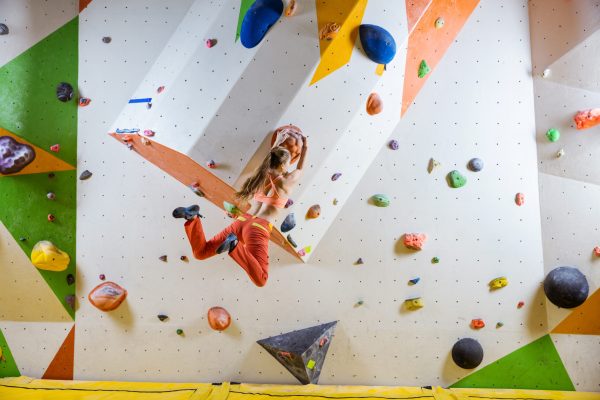 Young,Athletic,Woman,Jumping,On,Climbing,Hold,In,Bouldering,Gym
